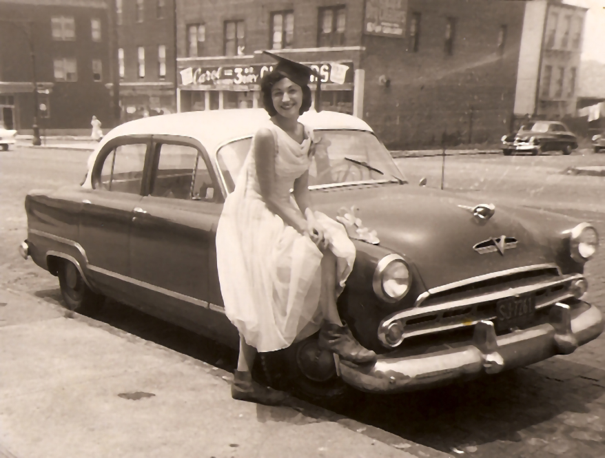 A young Marilyn in a beautiful dress, sitting gracefully on a car on her graduation day.