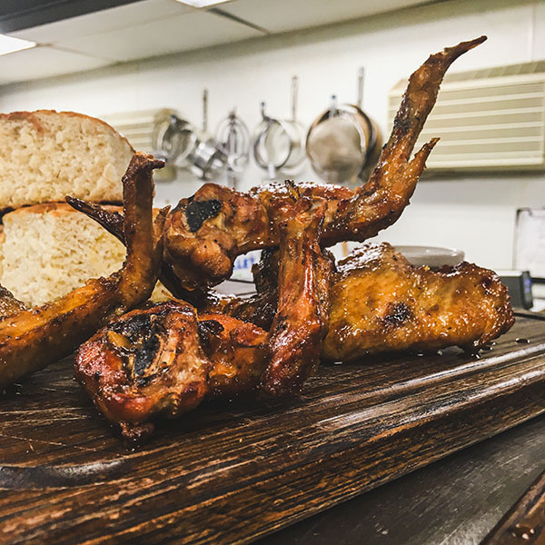 A wooden cutting board with chicken wings on top.