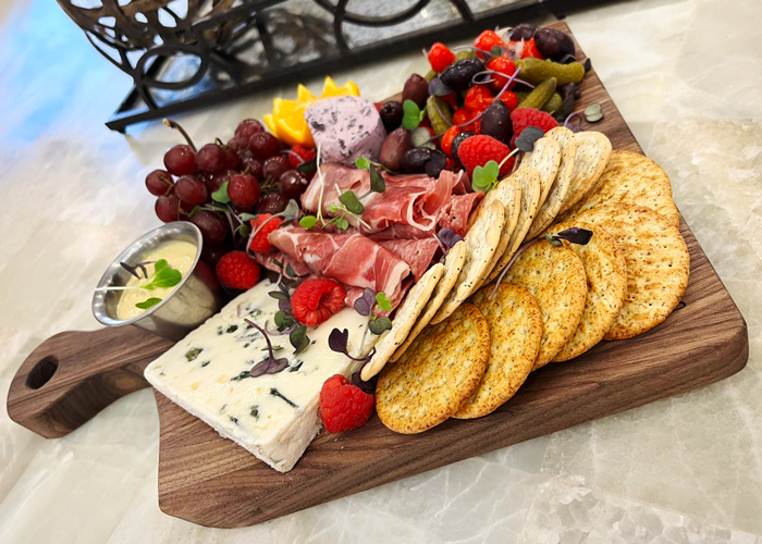 Charcuterie board with crackers, blue cheese, prosciutto, fresh grapes, raspberries, olives, pickles, and a side of mustard, artfully arranged for a gourmet snack or appetizer.