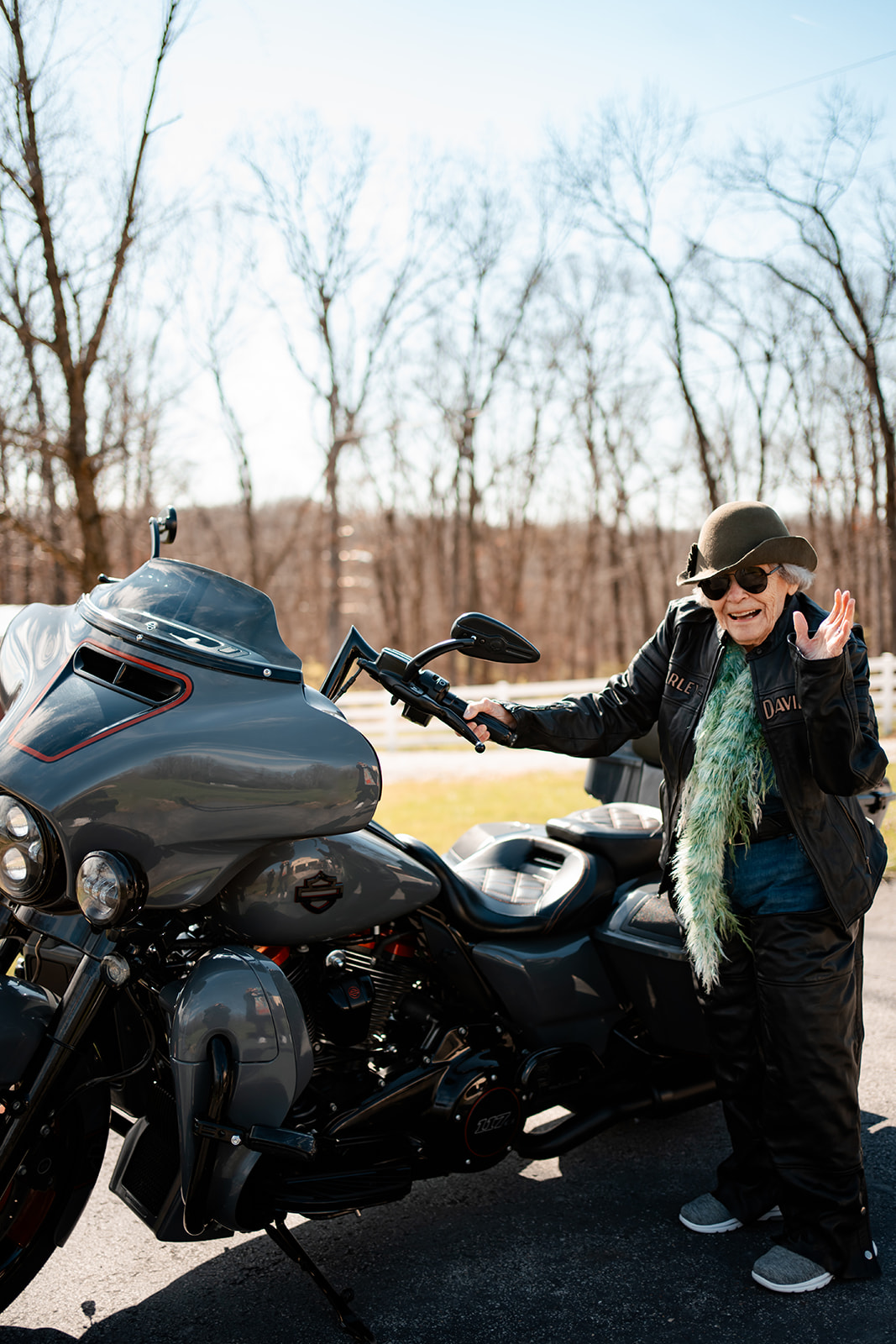 Senior resident wearing a stylish hat, sunglasses, and a Harley-Davidson jacket poses confidently next to a sleek motorcycle, exuding a spirited and adventurous vibe.