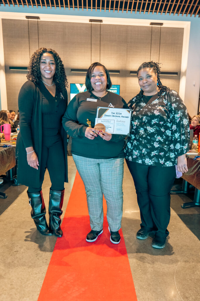 Three Arrow Senior Living team members pose on the "red carpet", one holding a certificate, at the 2025 Wellness summit.