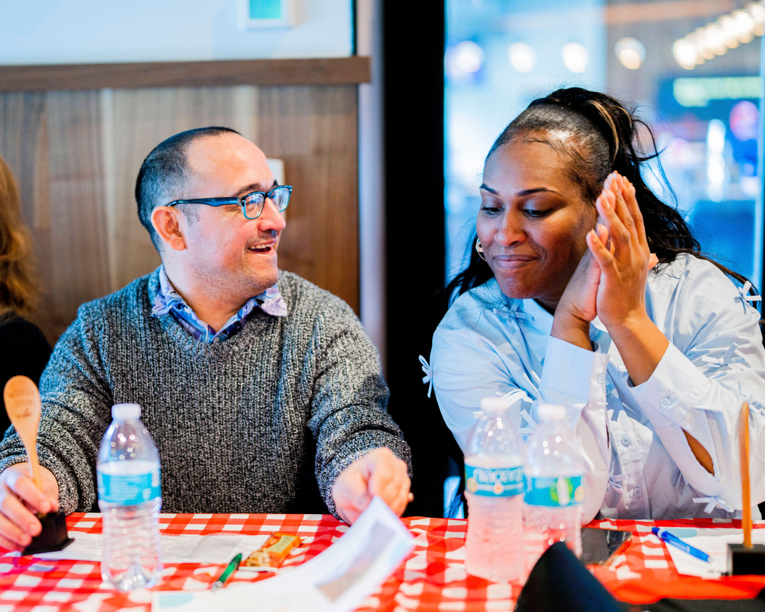 A man and a woman smile in conversation, seated together at a table covered with a checkered tablecloth during the 2025 Culinary summit.