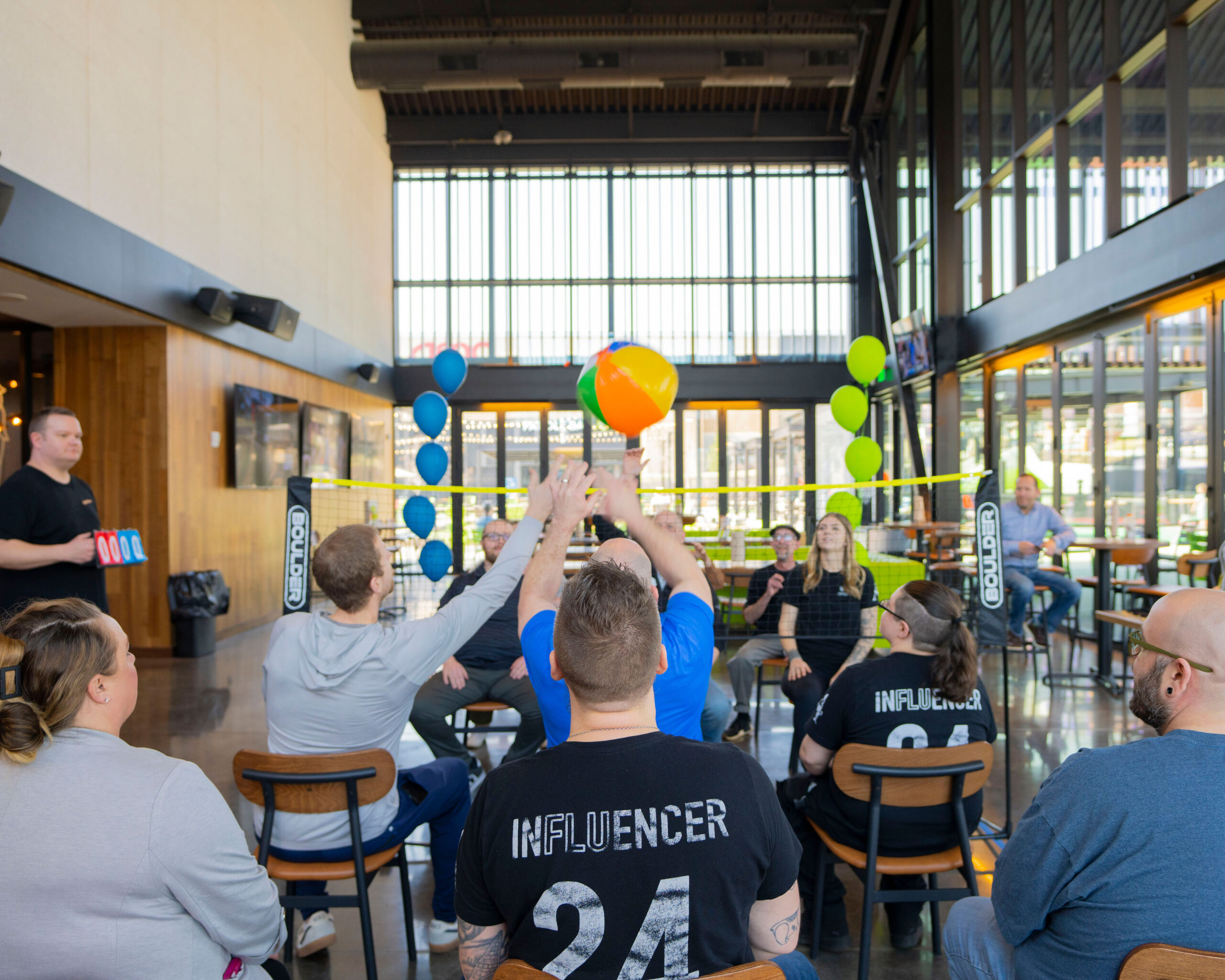 Arrow Senior Living team playing an indoor beach volleyball game during the 2025 Growth Summit, raising their hands and cheering as the ball goes over the net.