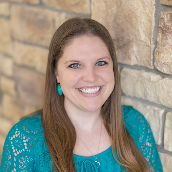 Heather Maxon, Resident Experience Coordinator for Arrow Senior Living, smiling in a teal blouse against a light stone wall background.