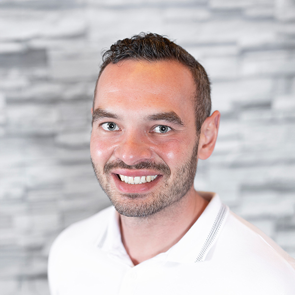 Chase Belza, Accounts Payable Specialist at Arrow Senior Living, smiling in a white collared shirt with a textured gray background behind him.