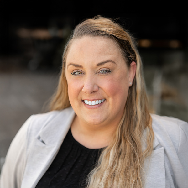 Christine Archery, Regional Culinary Coordinator at Arrow Senior Living, smiles in a light blazer and black top while standing outside with a blurred background.