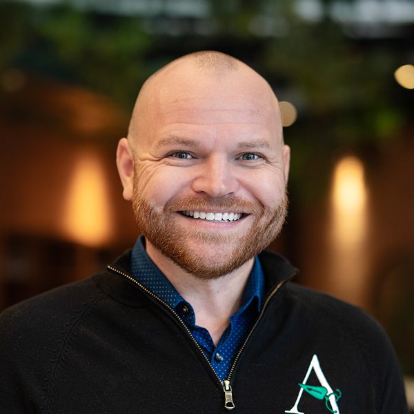 Derek Harris, Managing Director of Wellness Integrations at Arrow Senior Living, smiling in an Arrow jacket with a softly lit indoor background.