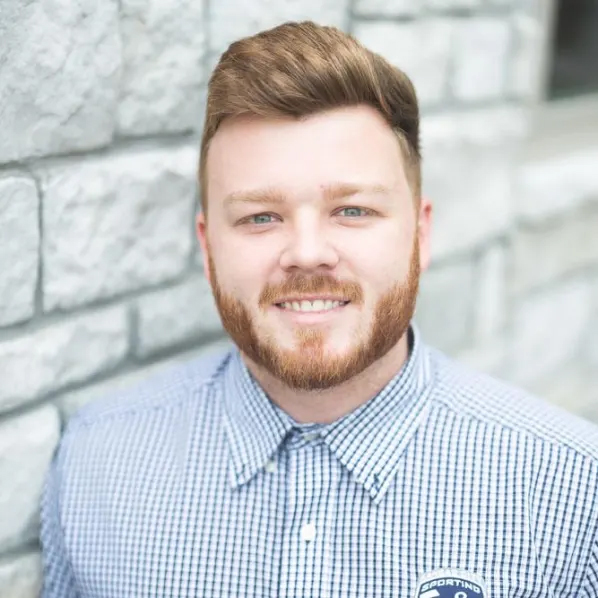 Coby Roark, Arrow Senior Living Director for the Kansas City market, smiling in a checkered button-up shirt, standing in front of a light gray brick wall.