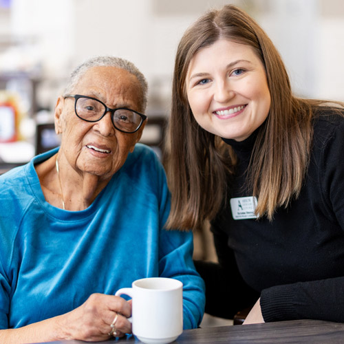 Resident Experience Director and senior woman smiling while enjoying a cup of coffee.