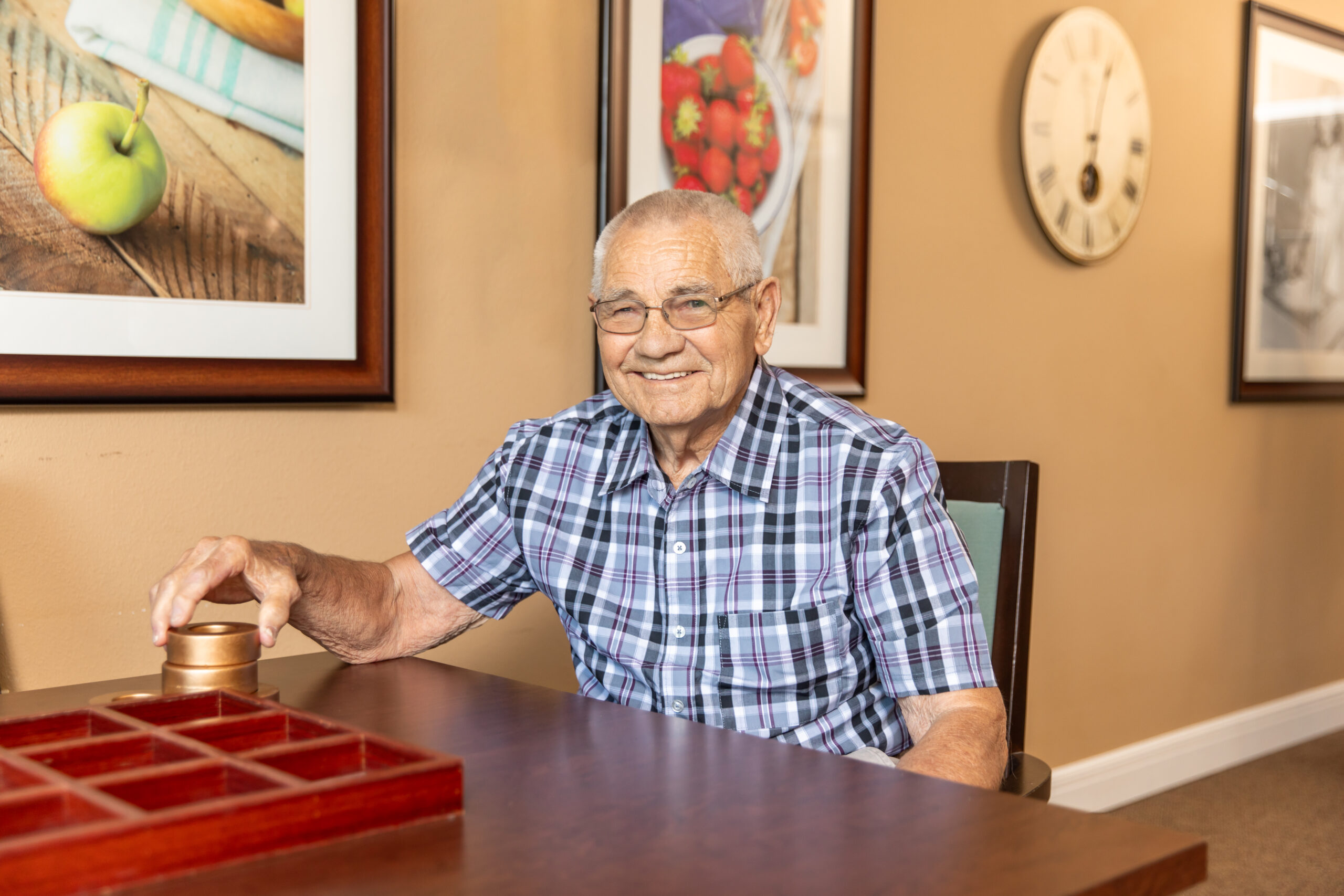 A senior resident smiling at a table while playing a wooden board game indoors, enjoying a friendly and engaging recreation activity.