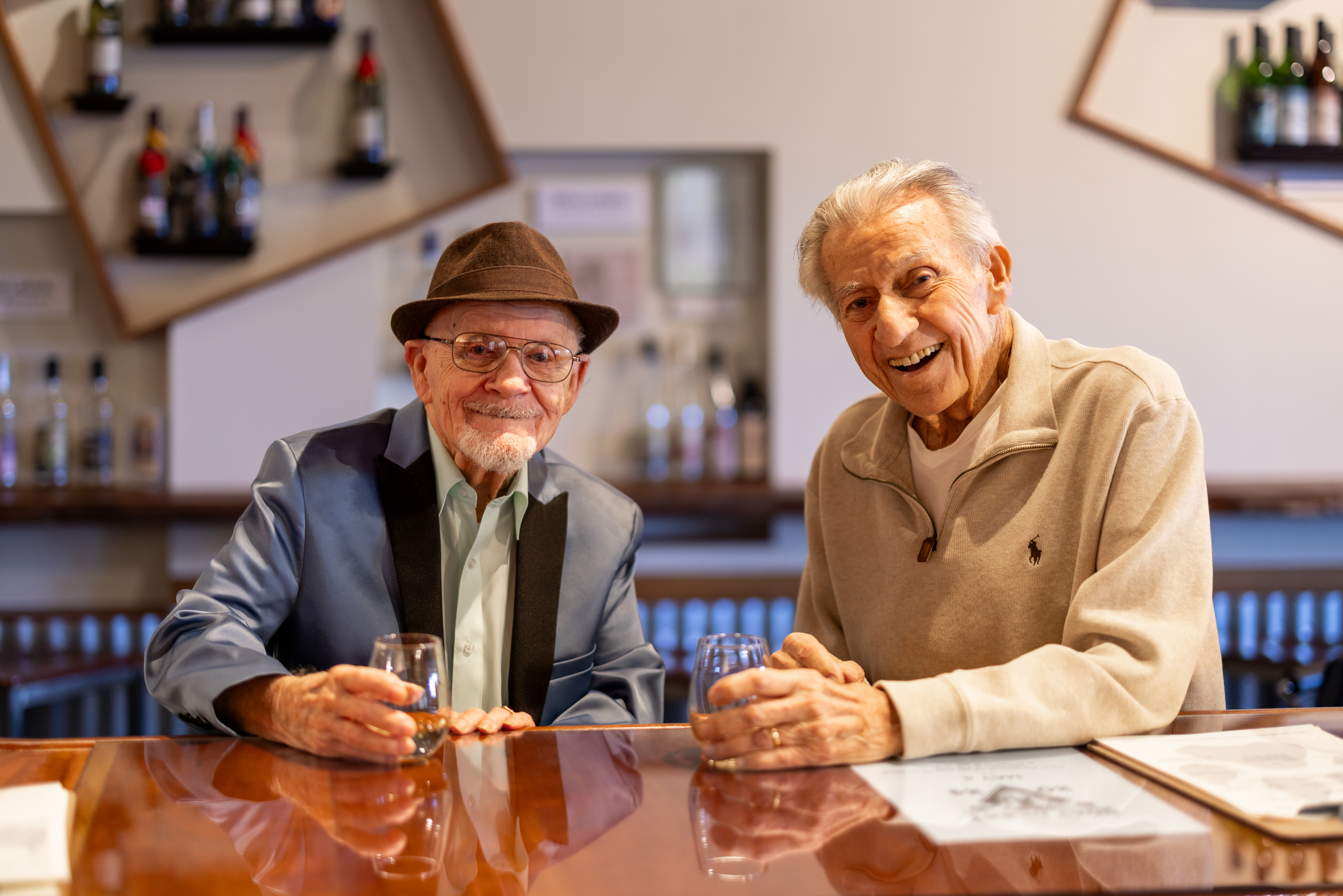 Two senior residents enjoying drinks at a community bar, smiling and sharing conversation during a social outing in a warm, welcoming setting.