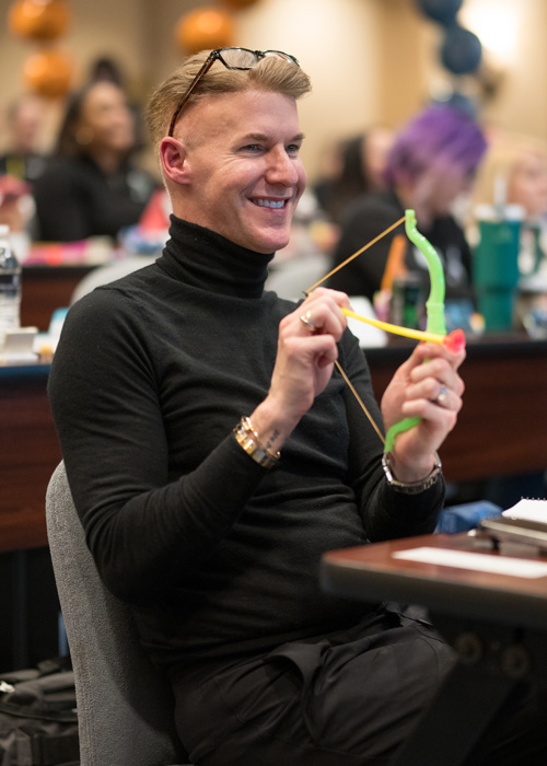 An Arrow Senior Living's Life Coach smiles while holding a toy bow during a lively 2025 Arrow Summit session filled with creativity, laughter, and team engagement.