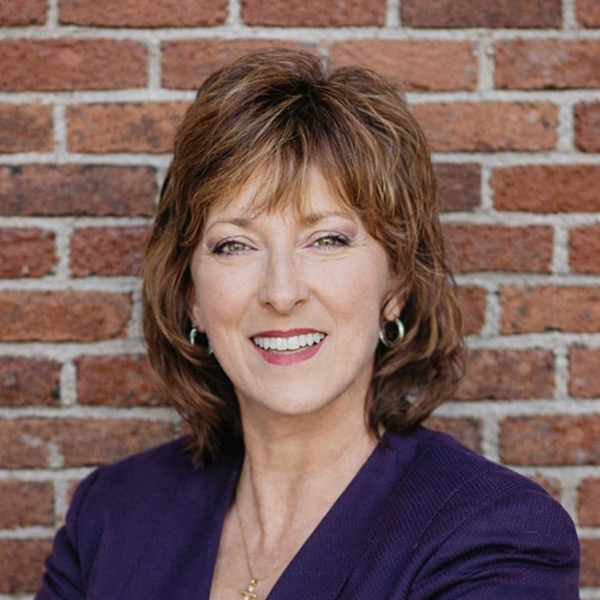 Becky Kaufmann, Managing Director of Wellness at Arrow Senior Living Home Office, smiling in a professional headshot, wearing a purple blazer, posed against a brick wall background.