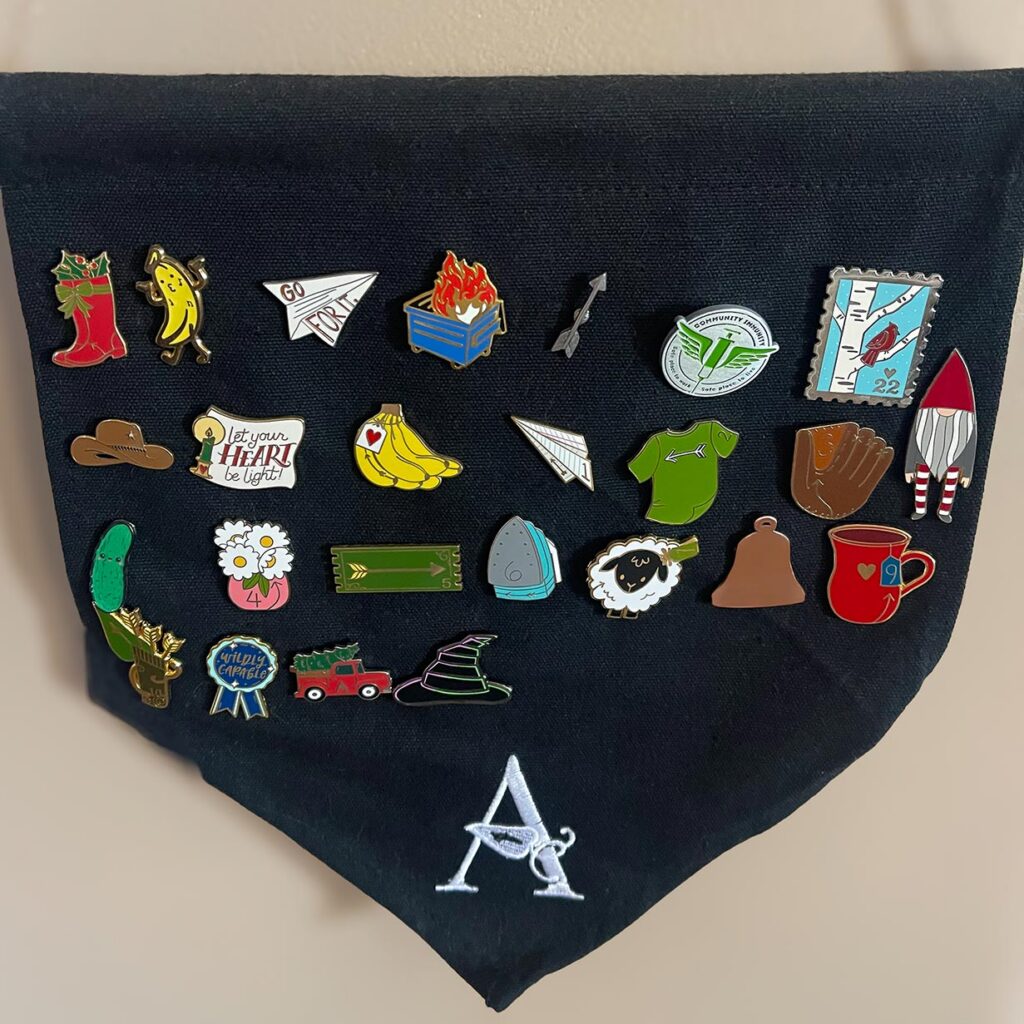 An assortment of colorful enamel pins alongside the Arrow Senior Living logo.