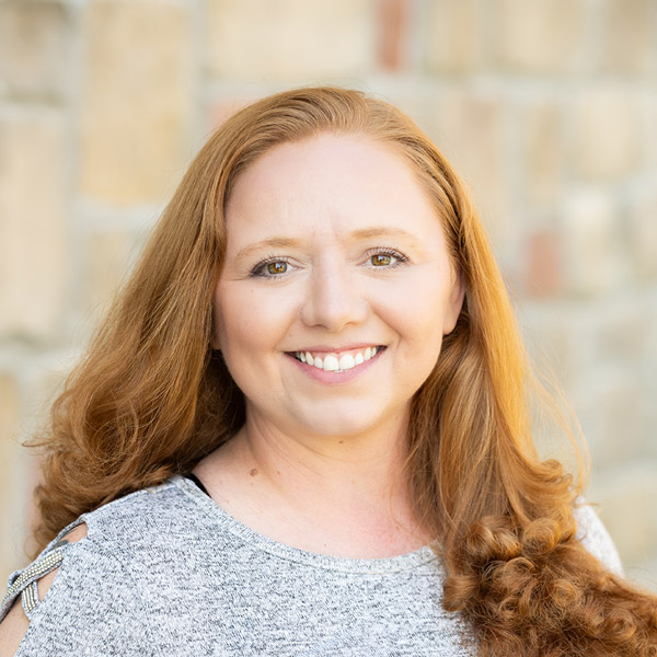 Brittney Rains, Resident Experience Coordinator at Arrow Senior Living, smiling in a professional headshot, wearing a gray top, with a softly blurred stone background.