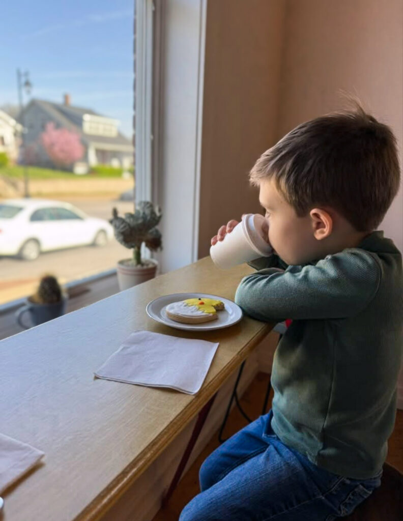 A child enjoys a beverage and snack at a local business, looking out at the world from a window.
