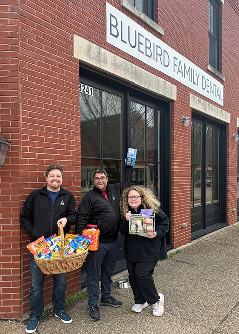 Three smiling members of Arrow Senior Living excitedly pose with gifts for a local dentistry office.