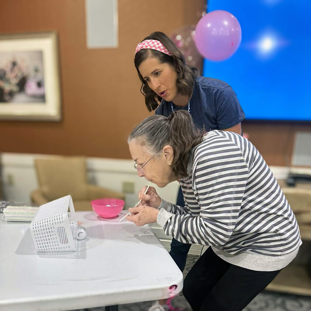 A young woman looks on while a senior woman engages in a game during a community event.