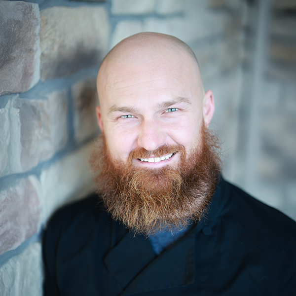 Robert Setina, Regional Plant Operations Director at Arrow Senior Living Home Office, smiling in a professional headshot, wearing a black jacket, with a softly blurred stone wall background.