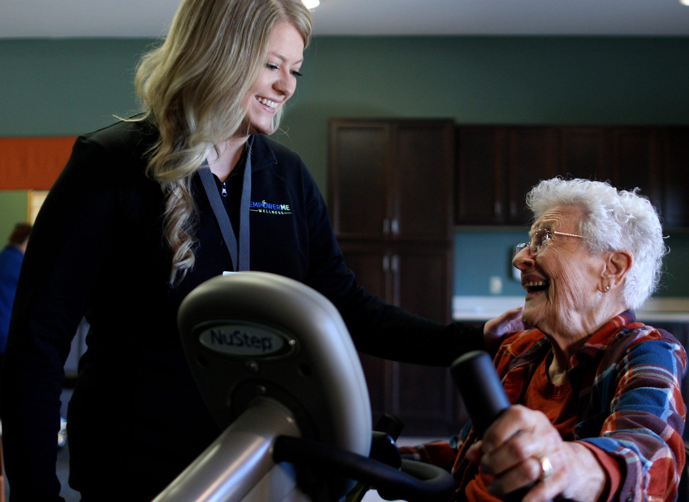 Wellness team member smiles with a resident using a NuStep machine during an exercise session.