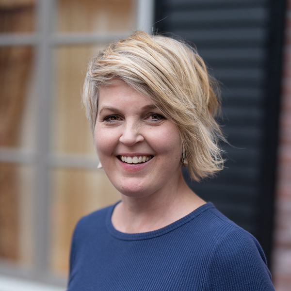 Krista Kruithoff, Regional Memory Care Coordinator at Arrow Senior Living Home Office, smiling in a professional headshot with short blonde layered hair, a blue top, and softly blurred window details in the background.