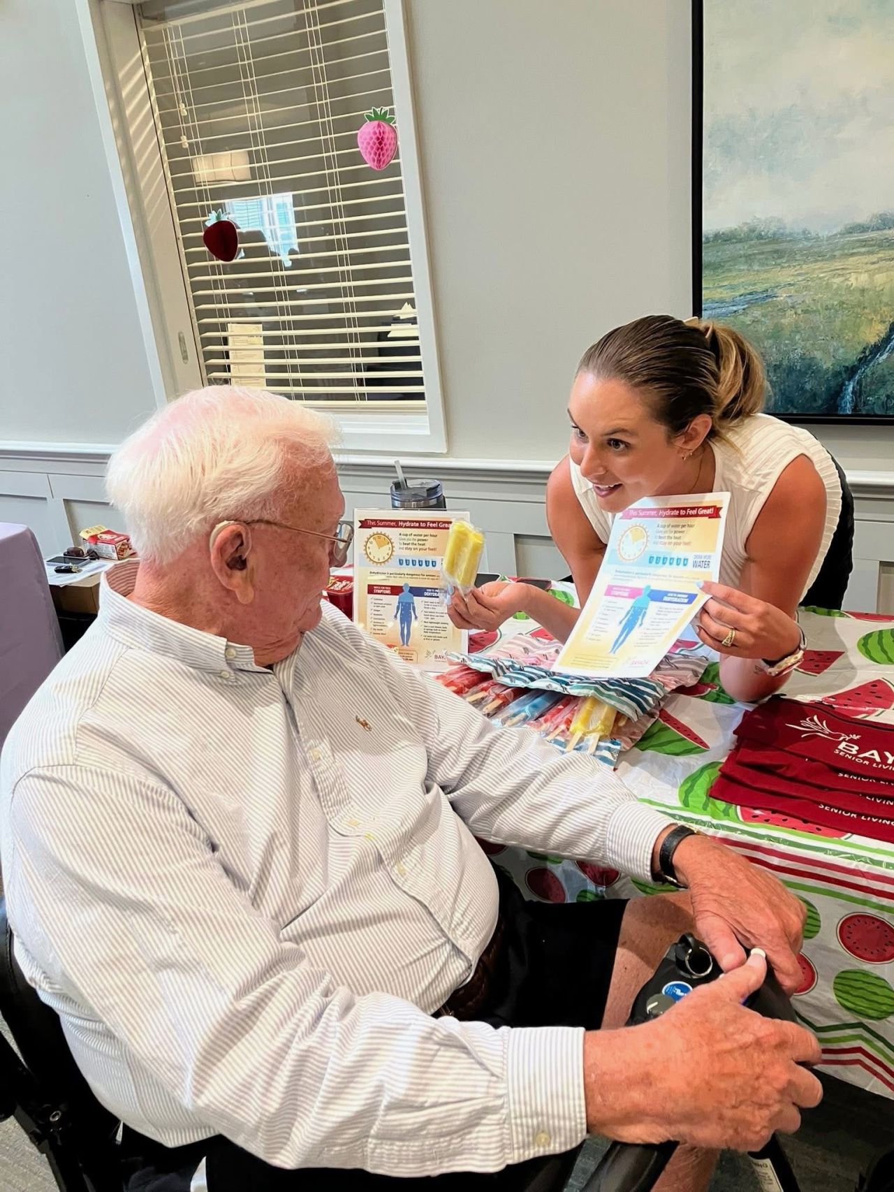 Team member shares summer hydration tips and a frozen treat with a resident during a wellness event at a senior living community.