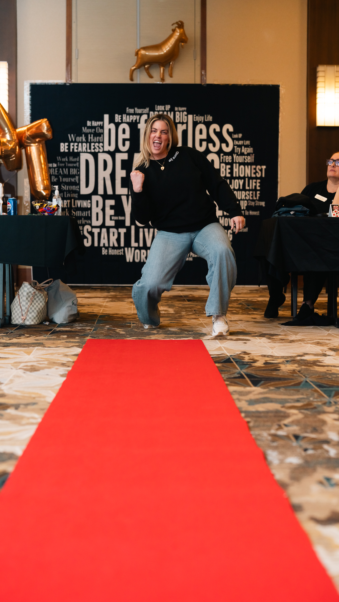 Arrow Senior Living team member poses on a red carpet in front of a motivational backdrop during a wellness event.
